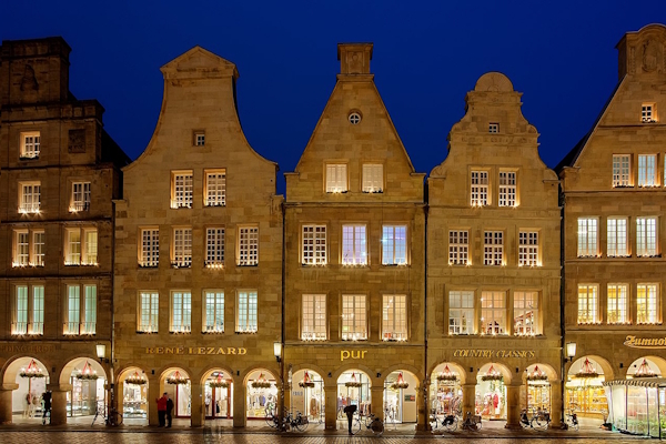 Abendaufnahme der beleuchteten Giebelhäuser am Prinzipalmarkt in Münster für Immobilienmakler FREIESLEBEN.